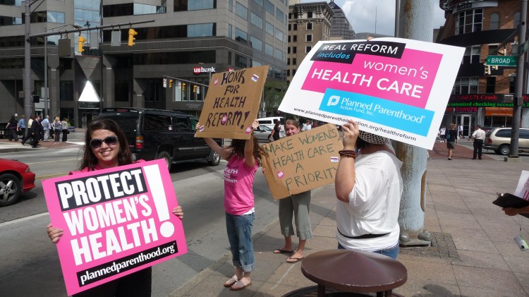 People standing on the side of a road holding up posters campaigning for health care.